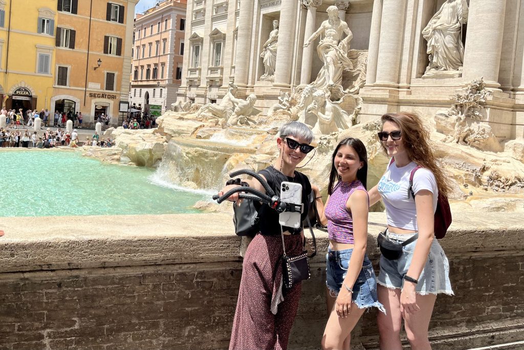 Three tourists with a selfie stick at Rome’s Trevi Fountain